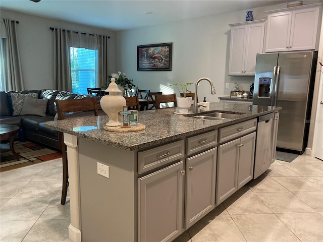 kitchen featuring gray cabinetry, sink, dark stone countertops, an island with sink, and stainless steel appliances