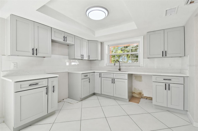 kitchen featuring gray cabinets, light tile patterned floors, sink, and a tray ceiling