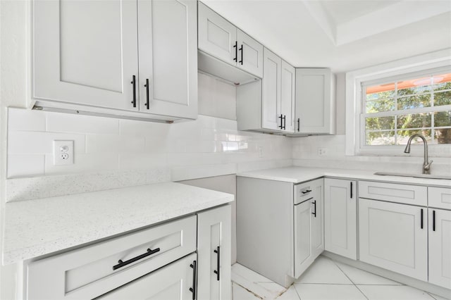 kitchen featuring backsplash, light stone countertops, light tile patterned floors, and sink