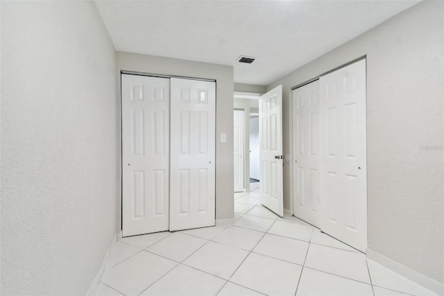 unfurnished bedroom with light tile patterned floors, a textured ceiling, and multiple closets