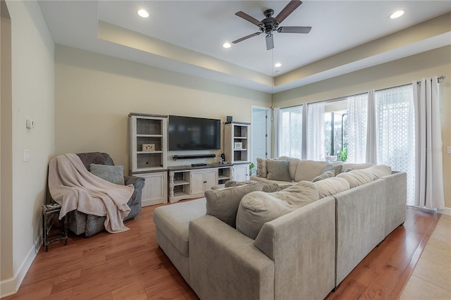 living room featuring light wood-type flooring, a raised ceiling, and ceiling fan