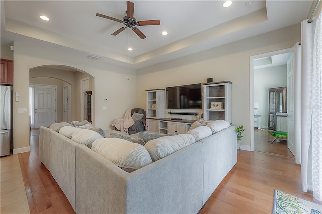 living room with ceiling fan, a tray ceiling, and light hardwood / wood-style flooring