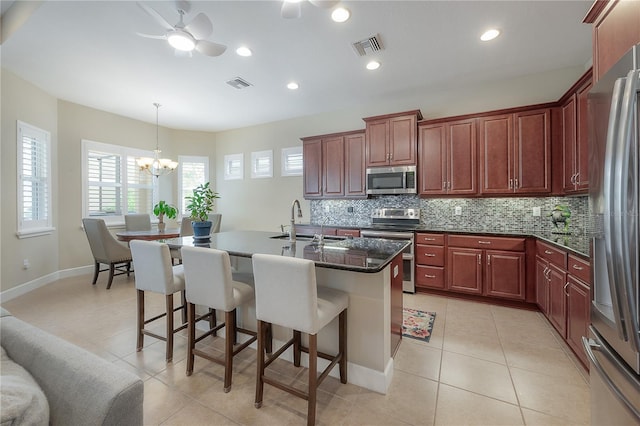 kitchen with tasteful backsplash, stainless steel appliances, sink, an island with sink, and light tile patterned flooring