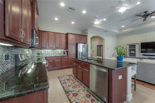 kitchen featuring a center island with sink, sink, decorative backsplash, light tile patterned floors, and stainless steel appliances