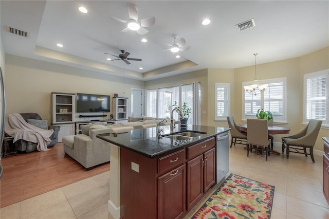 kitchen with stainless steel dishwasher, a raised ceiling, sink, light hardwood / wood-style flooring, and an island with sink