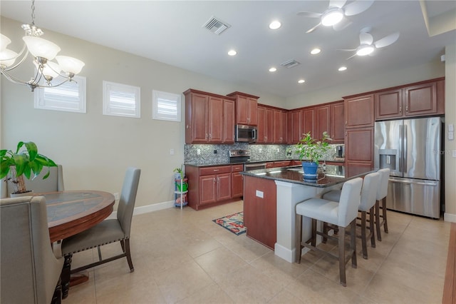 kitchen featuring backsplash, ceiling fan with notable chandelier, stainless steel appliances, a kitchen island, and hanging light fixtures