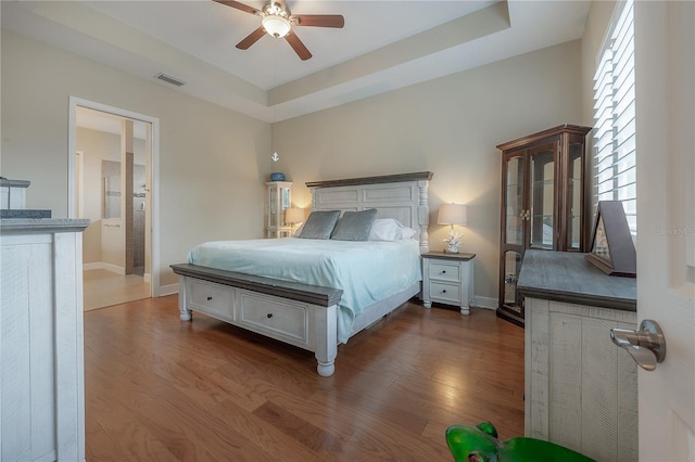 bedroom with connected bathroom, hardwood / wood-style flooring, ceiling fan, and a tray ceiling