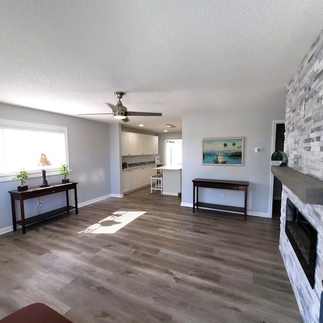 living room featuring a fireplace, a textured ceiling, dark hardwood / wood-style flooring, and ceiling fan