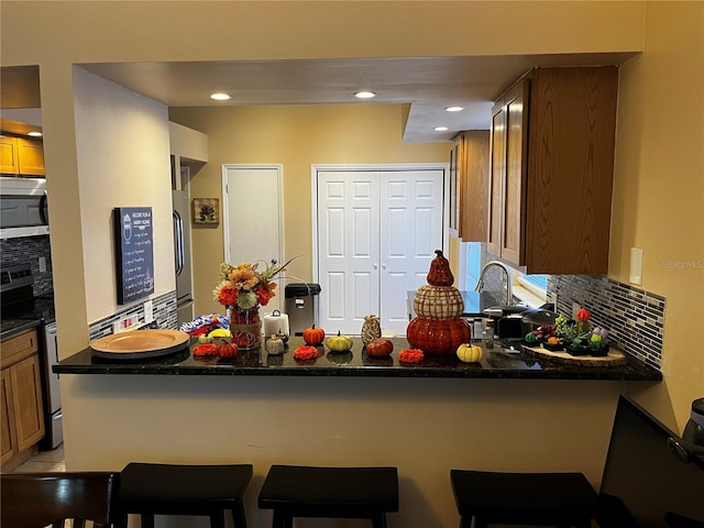 kitchen with a breakfast bar area, kitchen peninsula, stove, and backsplash