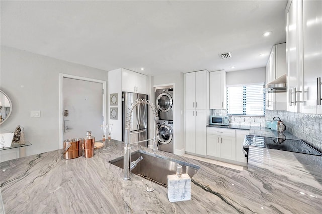 kitchen featuring light stone countertops, stainless steel appliances, white cabinetry, and stacked washer and clothes dryer