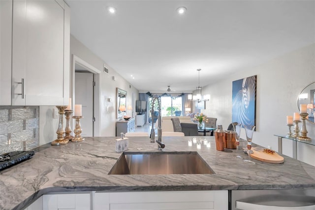 kitchen with white cabinets, ceiling fan with notable chandelier, light stone counters, and sink