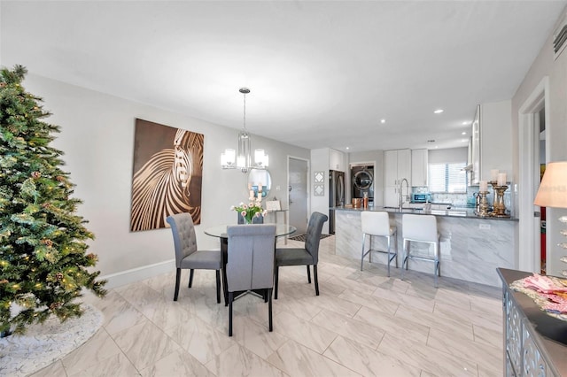 dining space featuring sink, stacked washer and clothes dryer, and an inviting chandelier