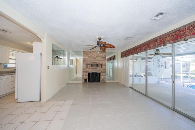 unfurnished living room featuring ceiling fan, a textured ceiling, and a brick fireplace