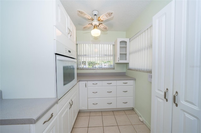 kitchen with a textured ceiling, ceiling fan, light tile patterned floors, oven, and white cabinetry