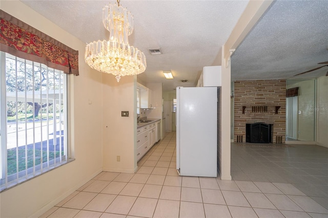 kitchen with pendant lighting, white fridge, a large fireplace, white cabinetry, and a chandelier