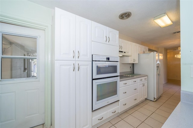 kitchen featuring a textured ceiling, white cabinets, light tile patterned flooring, and white appliances