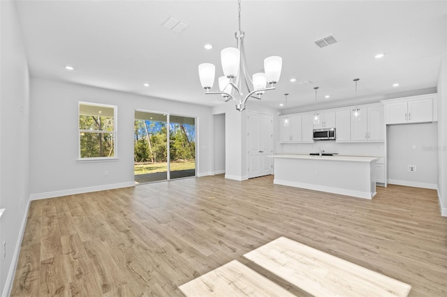 unfurnished living room featuring light wood-type flooring, an inviting chandelier, and sink