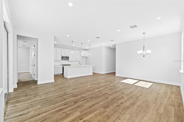 unfurnished living room featuring light wood-type flooring and an inviting chandelier