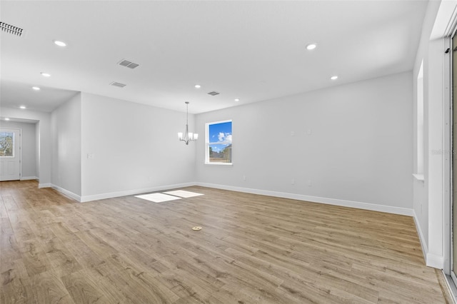 empty room featuring a chandelier, light hardwood / wood-style flooring, and a healthy amount of sunlight