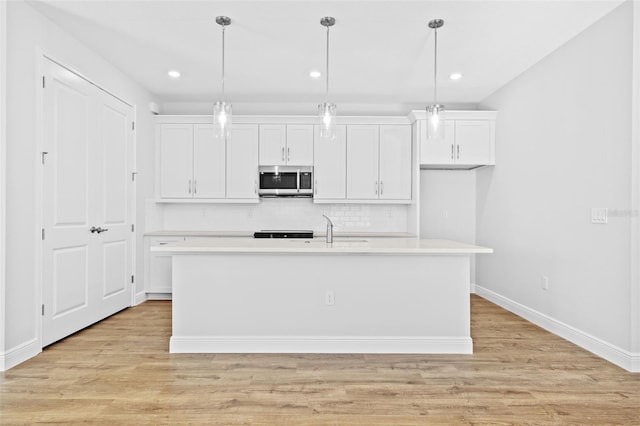 kitchen with white cabinets, decorative light fixtures, light wood-type flooring, and a kitchen island with sink