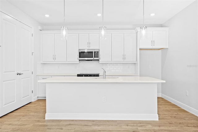 kitchen featuring white cabinets, an island with sink, hanging light fixtures, and light hardwood / wood-style flooring