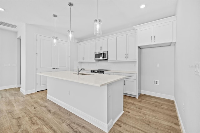 kitchen with light wood-type flooring, stainless steel appliances, a kitchen island with sink, decorative light fixtures, and white cabinetry