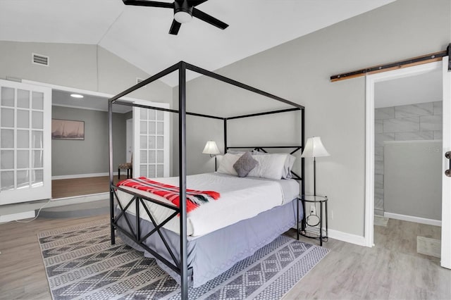 bedroom with lofted ceiling, hardwood / wood-style floors, a barn door, and ceiling fan