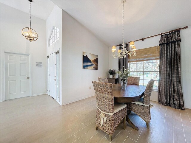 dining space featuring a chandelier, high vaulted ceiling, light wood-style flooring, and baseboards