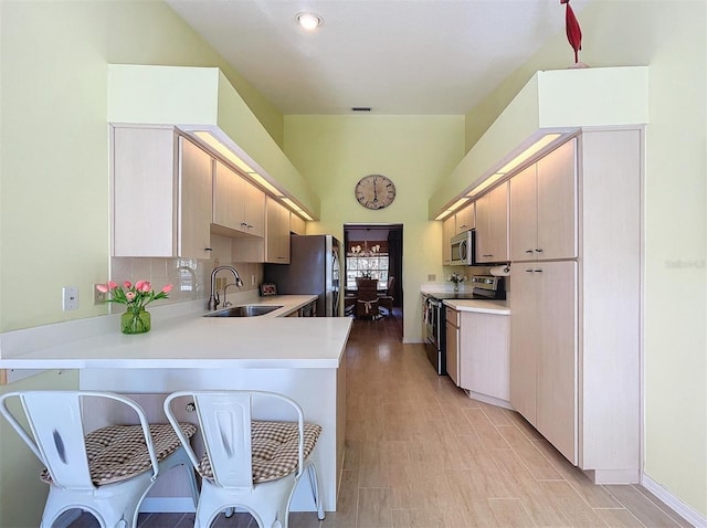 kitchen with stainless steel appliances, light countertops, light brown cabinets, a sink, and a peninsula