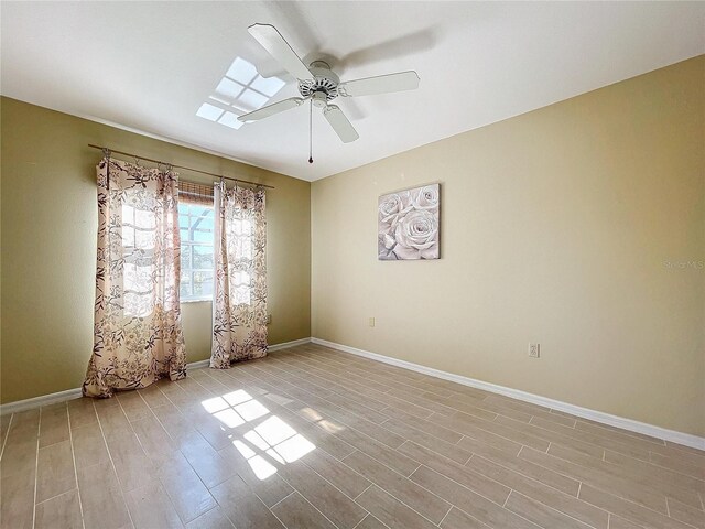 spare room with light wood-style floors, baseboards, a skylight, and a ceiling fan