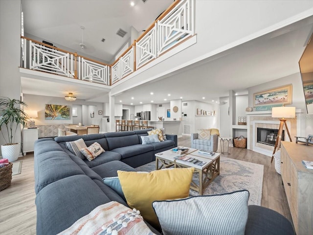 living room with a fireplace, light hardwood / wood-style flooring, and a high ceiling