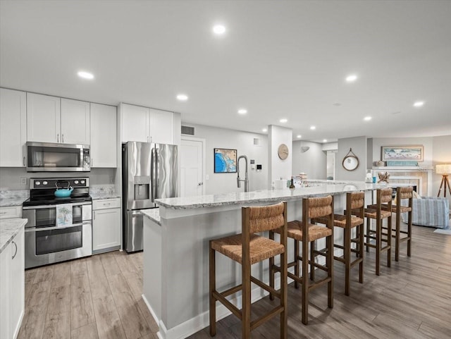 kitchen with white cabinetry, stainless steel appliances, a kitchen breakfast bar, an island with sink, and light wood-type flooring