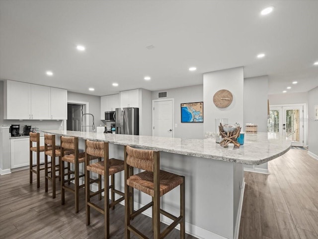 kitchen with appliances with stainless steel finishes, dark hardwood / wood-style floors, white cabinetry, and a breakfast bar area