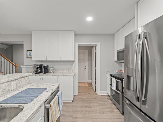 kitchen featuring white cabinetry, light stone countertops, light wood-type flooring, and stainless steel appliances