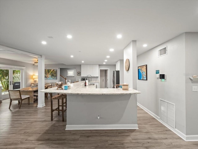 kitchen with a breakfast bar area, white cabinetry, a large island, and hardwood / wood-style flooring