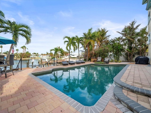 view of pool with a patio area, a water view, and a dock