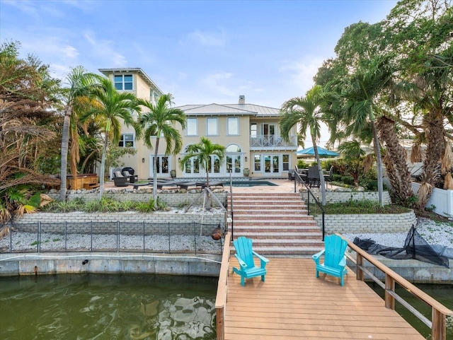 dock area with a balcony, a water view, and a patio