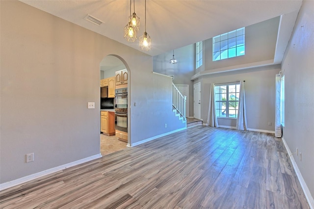 unfurnished living room with light wood-type flooring, a towering ceiling, and an inviting chandelier