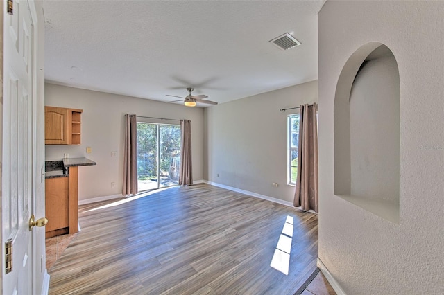 unfurnished living room with ceiling fan, light wood-type flooring, and a textured ceiling