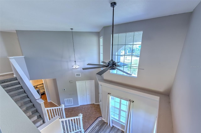 stairway with ceiling fan, a towering ceiling, and wood-type flooring