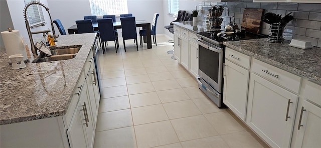 kitchen featuring light stone countertops, tasteful backsplash, sink, white cabinets, and stainless steel electric range