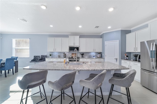 kitchen featuring a center island with sink, white cabinets, crown molding, appliances with stainless steel finishes, and light stone counters