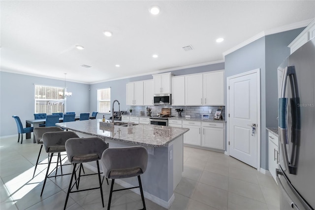 kitchen with white cabinetry, sink, stainless steel appliances, decorative light fixtures, and a kitchen island with sink