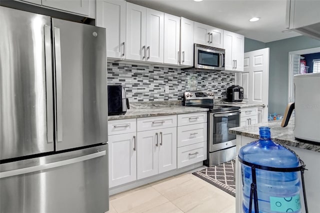 kitchen featuring backsplash, light tile patterned floors, light stone countertops, appliances with stainless steel finishes, and white cabinetry