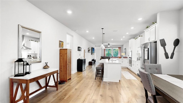 kitchen featuring pendant lighting, ceiling fan, a center island with sink, and white cabinets