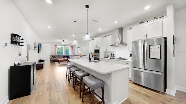 kitchen featuring appliances with stainless steel finishes, an island with sink, sink, white cabinets, and wall chimney exhaust hood