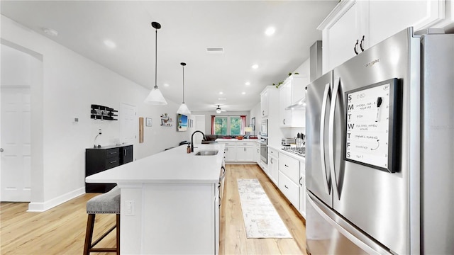 kitchen featuring appliances with stainless steel finishes, a kitchen breakfast bar, an island with sink, pendant lighting, and white cabinets