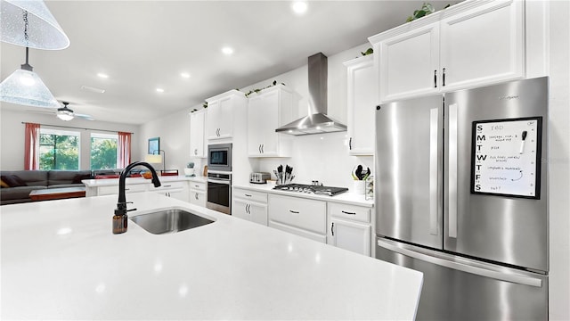 kitchen with decorative light fixtures, sink, white cabinets, stainless steel appliances, and wall chimney range hood