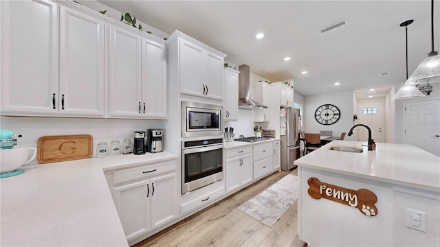 kitchen featuring sink, wall chimney range hood, white cabinetry, hanging light fixtures, and stainless steel appliances