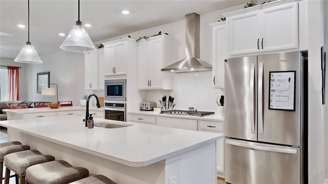 kitchen featuring stainless steel appliances, an island with sink, a breakfast bar area, and wall chimney range hood